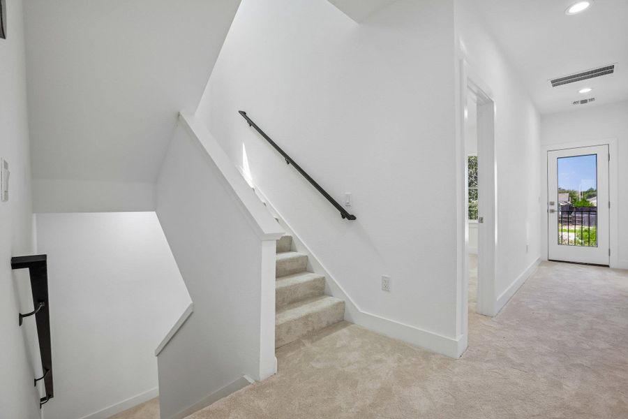 Crisp white walls and plush carpeting frame this multi-level staircase leading to a bright hallway.