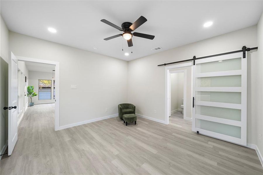 Unfurnished room with a barn door, light wood-type flooring, and ceiling fan