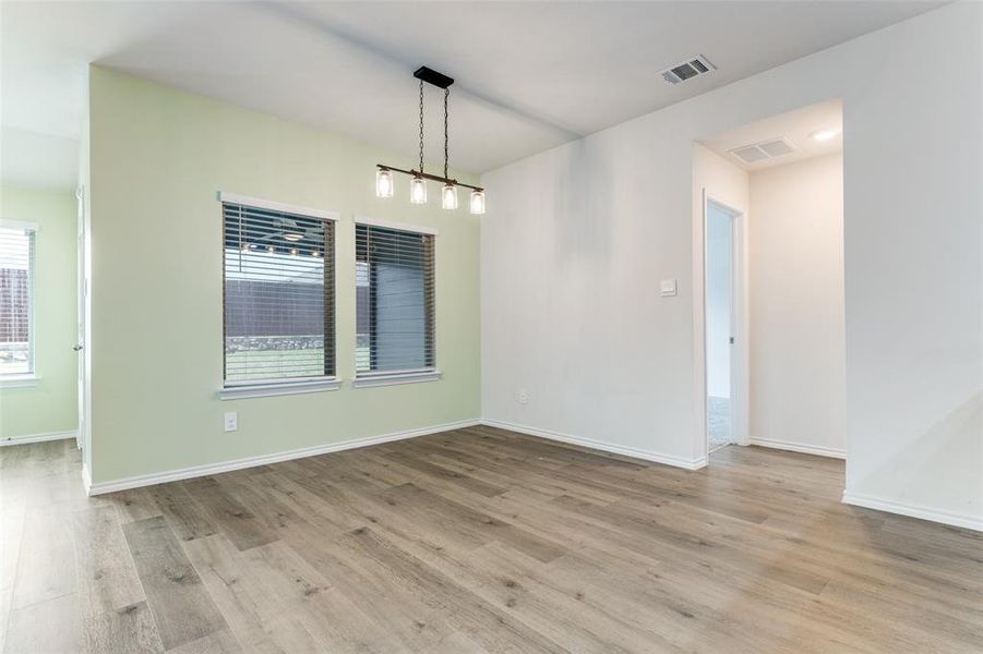 Bright interior space with wood-finish flooring, light green accent wall, multiple windows with blinds, and a contemporary linear chandelier with glass shades Bright interior space with wood-finish flooring, light green accent wall, multiple windows with blinds, and a contemporary linear chandelier with glass shades