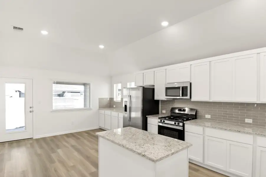 Kitchen featuring stainless steel appliances, white cabinetry, backsplash, light wood-style flooring, and a kitchen island