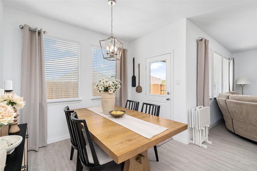The dining area features a light wood table, black chairs, and a contemporary chandelier