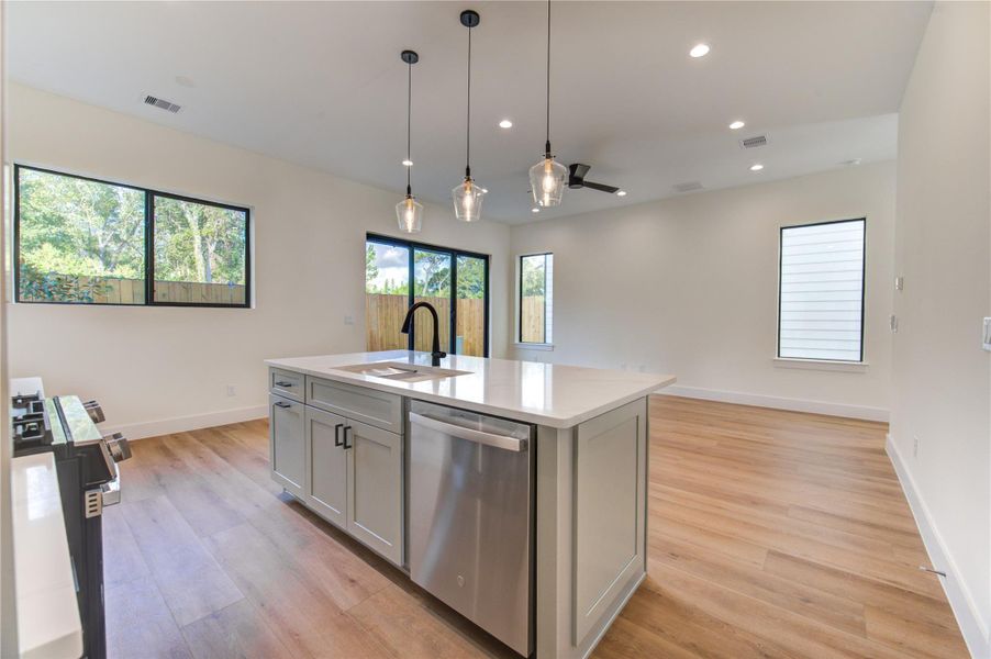 This modern open-plan kitchen and living area features sleek flooring, a large central island with a sink, pendant lighting, and ample natural light from large windows. This modern open-plan kitchen and living area features sleek flooring, a large central island with a sink, pendant lighting, and ample natural light from large windows.