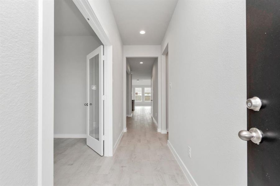 The grand entrance beckons with high ceilings, adorned with elegant wood-look tile flooring and oversized baseboards, and recessed lighting.  Follow path of natural light from expansive windows ahead. Sample photo of completed home with similar floor plan. As-built interior colors and selections may vary.