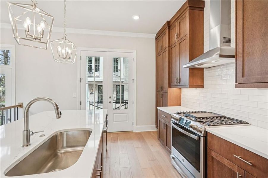 Kitchen featuring stainless steel gas range, wood finish cabinets, french doors, crown molding, and light stone countertops