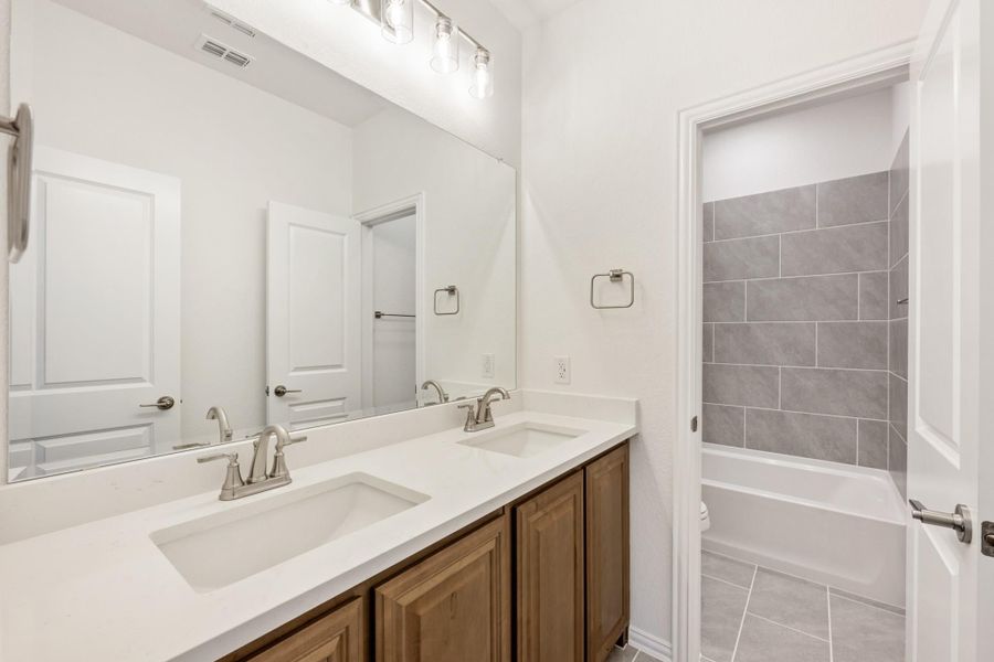 Bathroom with double sink vanity, wood cabinets, white countertop, and tiled shower-tub combo Bathroom with double sink vanity, wood cabinets, white countertop, and tiled shower-tub combo