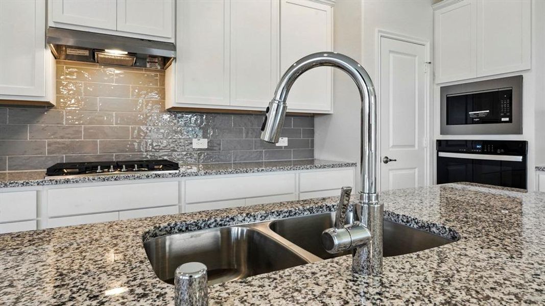 Kitchen featuring a double basin stainless steel sink with a high-arc faucet, granite countertops, white cabinetry, and a gray subway tile backsplash Kitchen featuring a double basin stainless steel sink with a high-arc faucet, granite countertops, white cabinetry, and a gray subway tile backsplash