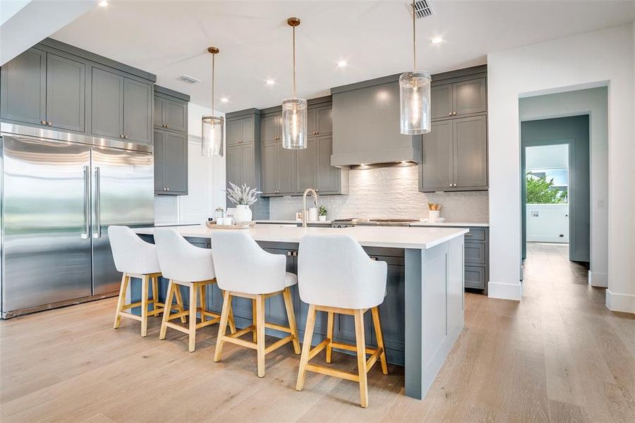 Kitchen with gray cabinets, stainless steel built in fridge, a kitchen bar, a kitchen island with sink, and recessed lighting