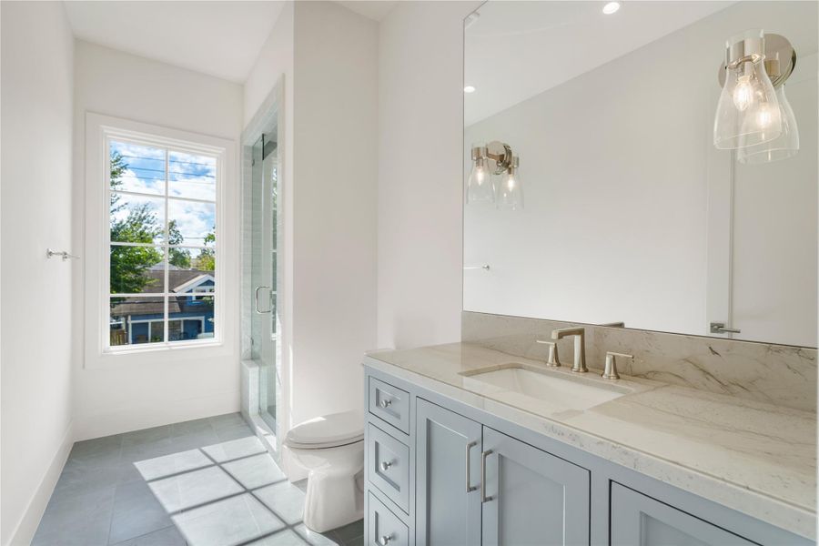 Light gray cabinets and beige quartz countertops combine to create a picturesque vanity in this bedroom’s en suite bathroom. The window floods the room with light and makes the polished nickel fixtures gleam.