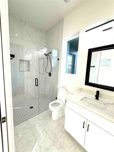 Bathroom featuring vanity, a marble finish shower, and light marble finish floors