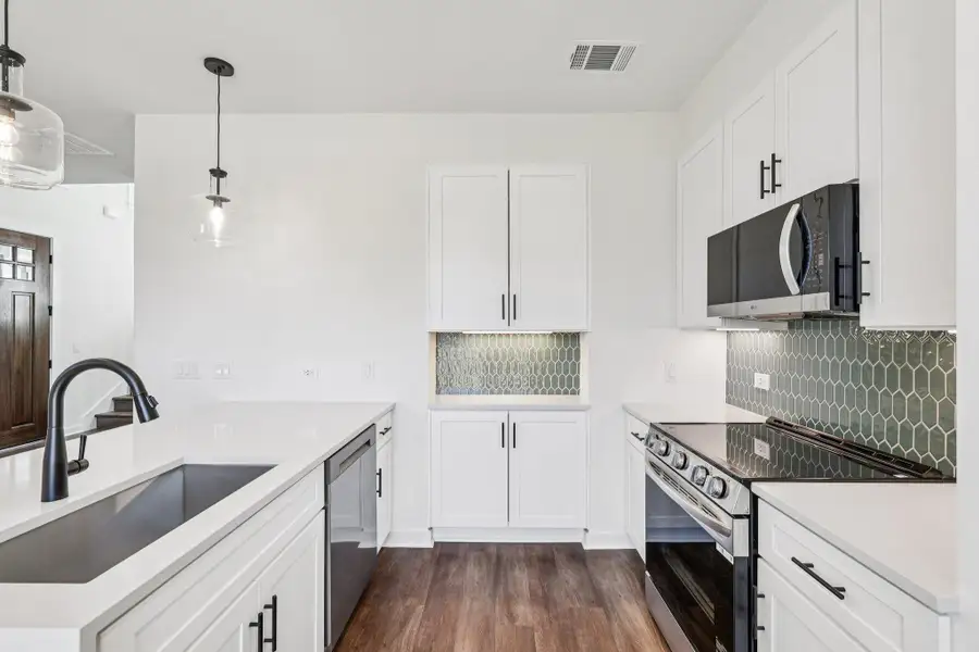 Kitchen with appliances with stainless steel finishes, white cabinetry, dark wood-style floors, decorative light fixtures, and backsplash Kitchen with appliances with stainless steel finishes, white cabinetry, dark wood-style floors, decorative light fixtures, and backsplash