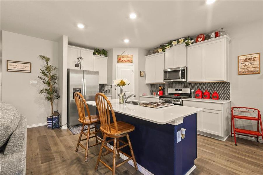 Kitchen with tasteful backsplash, stainless steel appliances, a kitchen bar, white cabinets, and recessed lighting Kitchen with tasteful backsplash, stainless steel appliances, a kitchen bar, white cabinets, and recessed lighting