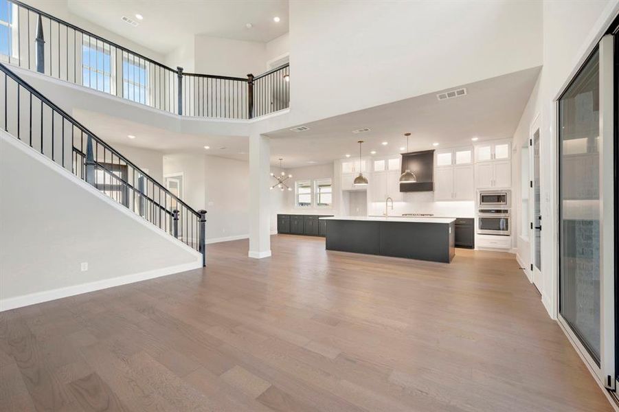 Unfurnished living room with light wood-style flooring, a chandelier, and a high ceiling Unfurnished living room with light wood-style flooring, a chandelier, and a high ceiling