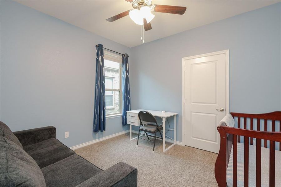 Bedroom featuring light carpet, a nursery area, and ceiling fan