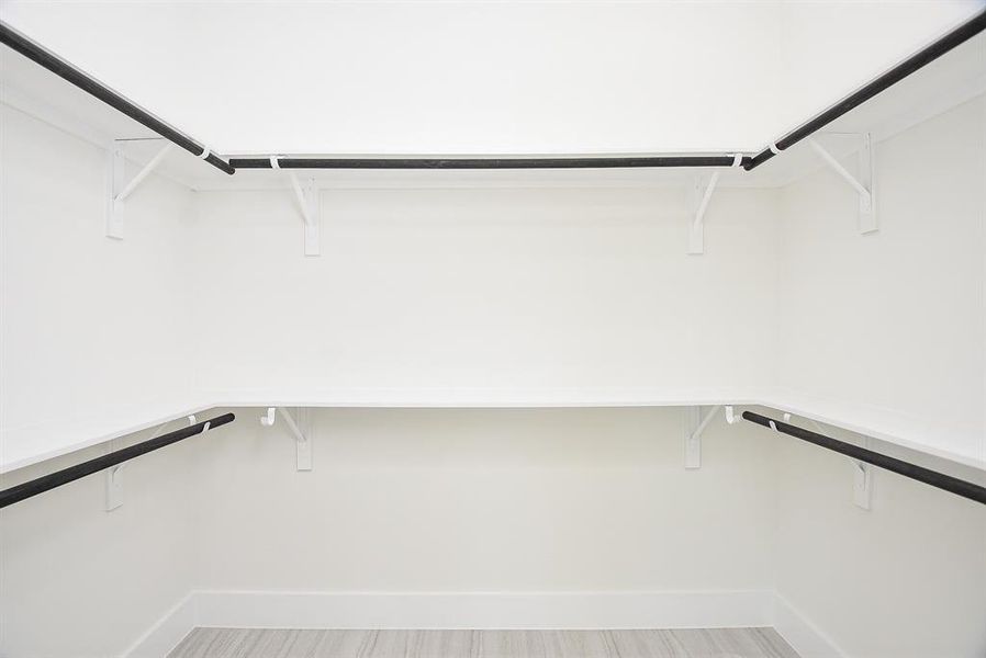 Spacious walk-in primary closet featuring built-in shelving and ample hanging space. Designed for optimal organization, this closet offers both style and functionality.