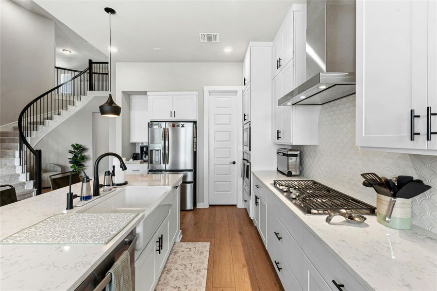 Kitchen with light stone counters, soft close white cabinets, light wood-style floors, and upgraded hanging light fixtures