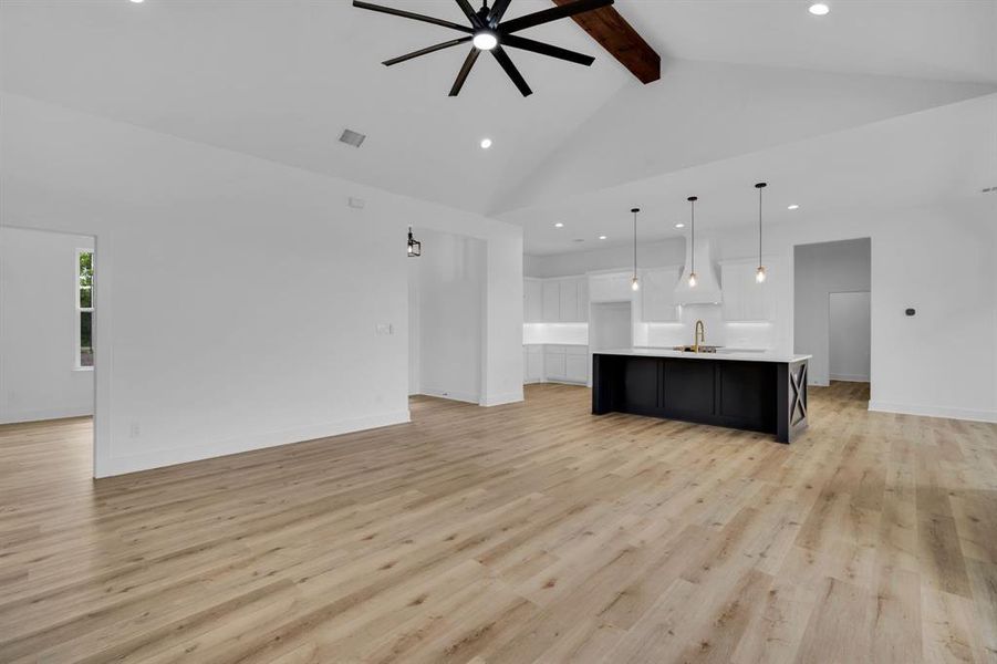 Unfurnished living room featuring beamed ceiling, light wood-type flooring, sink, and high vaulted ceiling