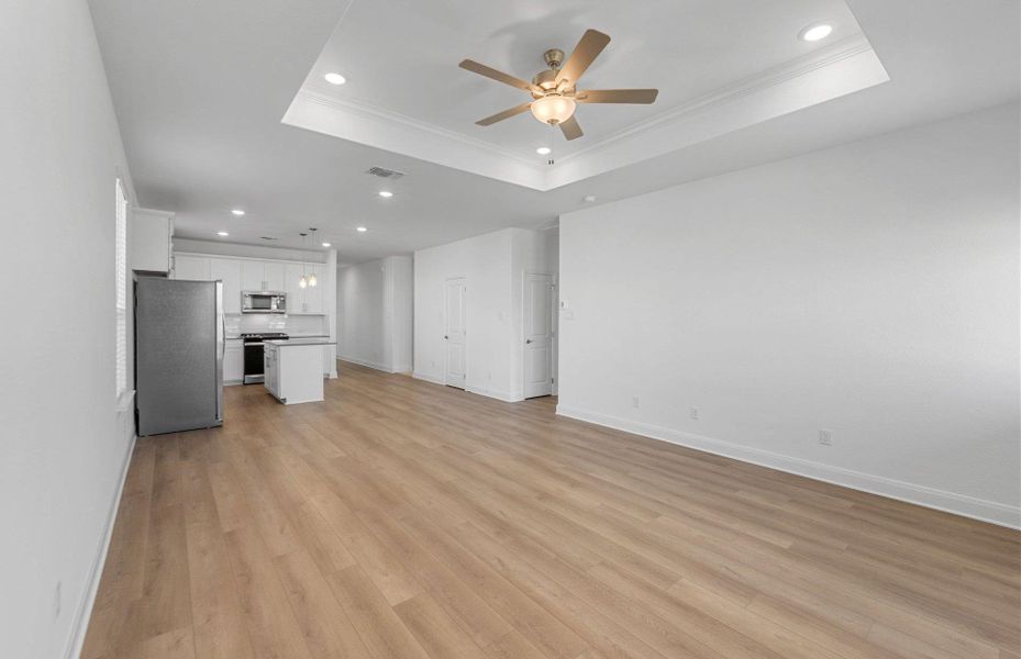 Unfurnished living room with a raised ceiling, light wood-type flooring, crown molding, recessed lighting, and ceiling fan