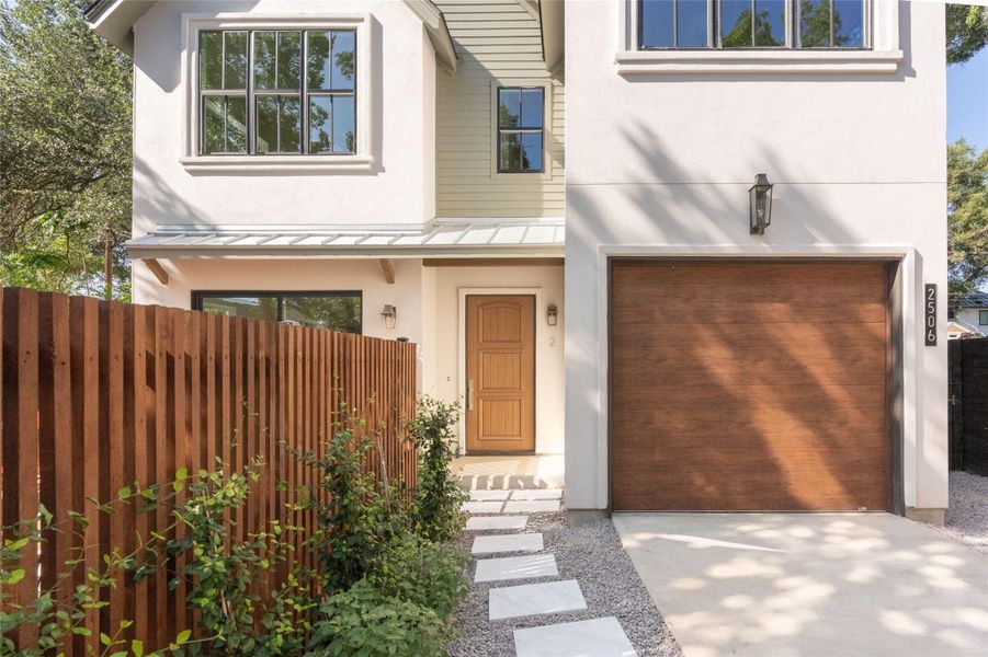 A modern facade with a natural wood garage door and privacy fence welcomes you home.