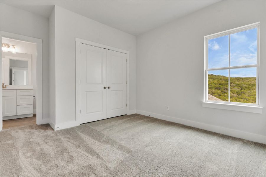 A spacious secondary bedroom features soft carpeting, ample closet space, and a window with vibrant hill country views.