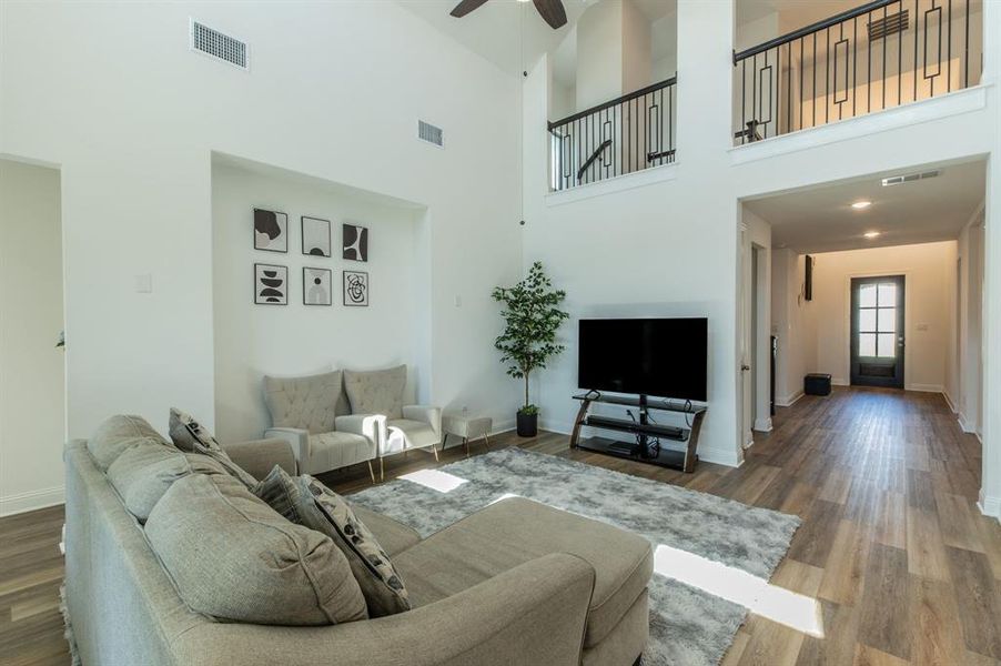 Two-story living area featuring vaulted ceilings, wood-finish flooring, a ceiling fan, and an open second-story walkway with black metal railing