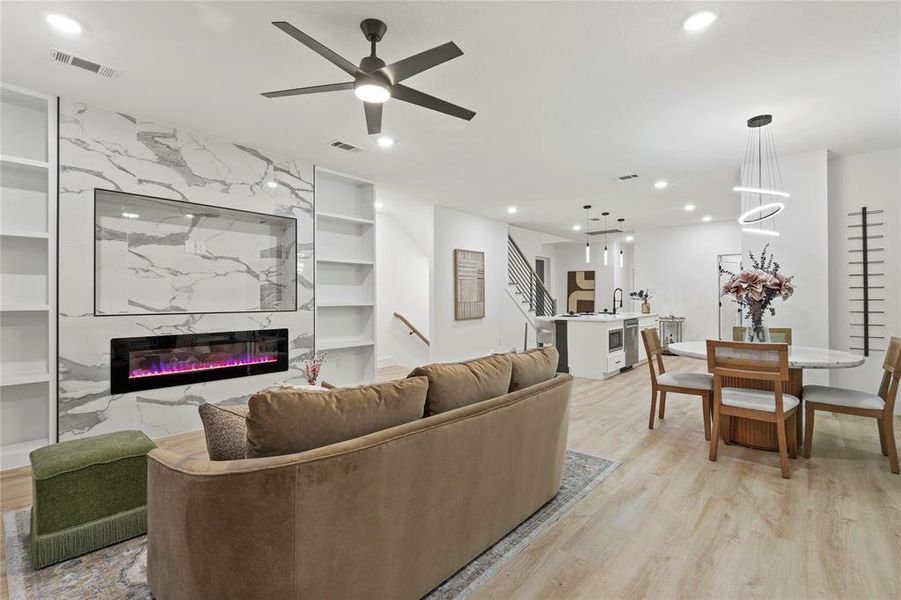 Living room featuring built in features, a fireplace, a ceiling fan, light wood-type flooring, and stairway Living room featuring built in features, a fireplace, a ceiling fan, light wood-type flooring, and stairway
