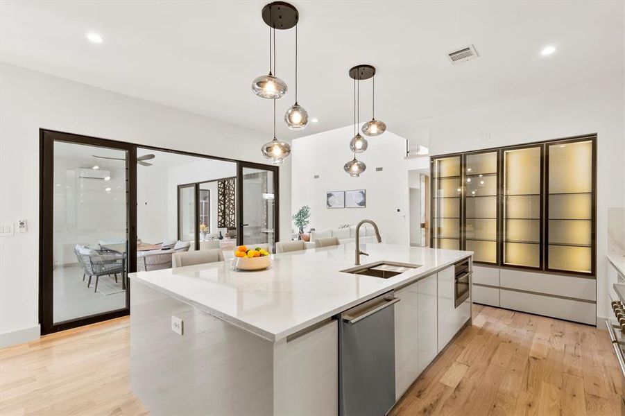 Kitchen with hanging light fixtures, stainless steel dishwasher, sink, and an island with sink