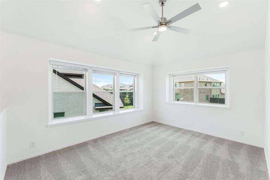 Empty bedroom with gray carpet, ceiling fan, and multiple windows overlooking neighboring homes Empty bedroom with gray carpet, ceiling fan, and multiple windows overlooking neighboring homes
