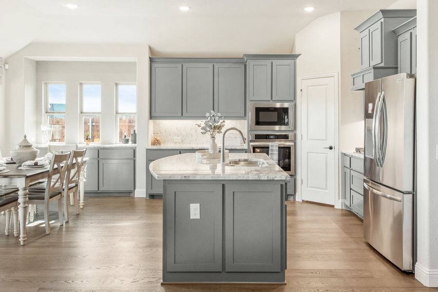 Kitchen with gray cabinets, center island with sink, stainless steel appliances, and hardwood floors open to dining area