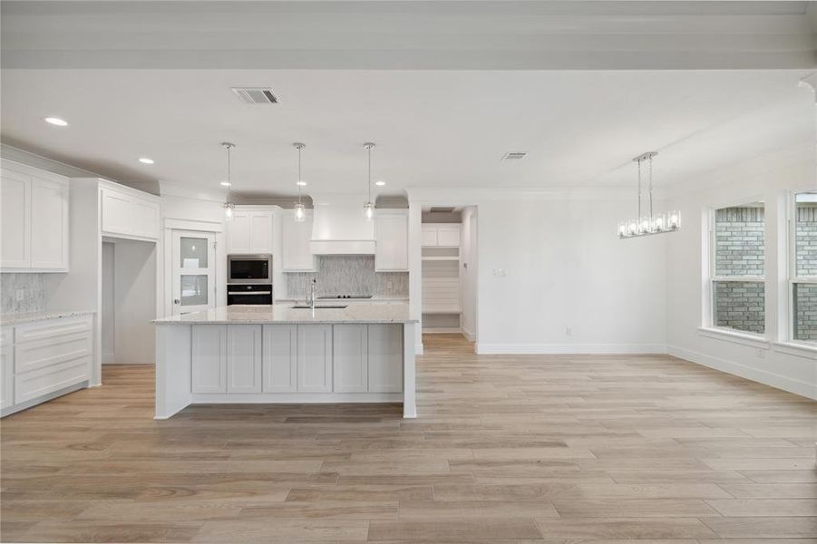 Kitchen with oven, stainless steel microwave, backsplash, and white cabinets