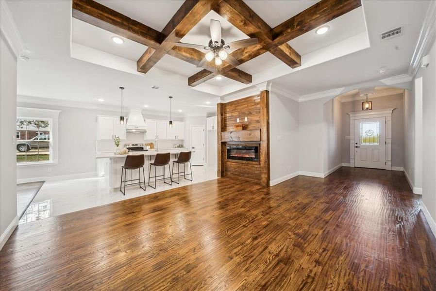 Unfurnished living room with beam ceiling, a large fireplace, ceiling fan, crown molding, and coffered ceiling