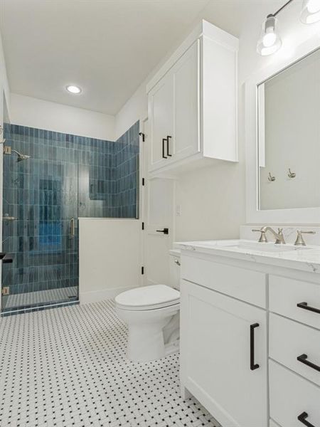 Bathroom featuring a glass-enclosed shower with blue vertical tile, white vanity with a light-toned countertop, white cabinetry with black hardware, and mosaic tile flooring Bathroom featuring a glass-enclosed shower with blue vertical tile, white vanity with a light-toned countertop, white cabinetry with black hardware, and mosaic tile flooring