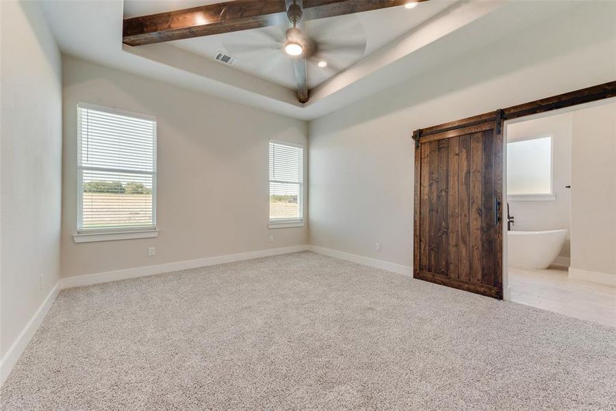 Carpeted empty room with beam ceiling, a barn door, a raised ceiling, and ceiling fan