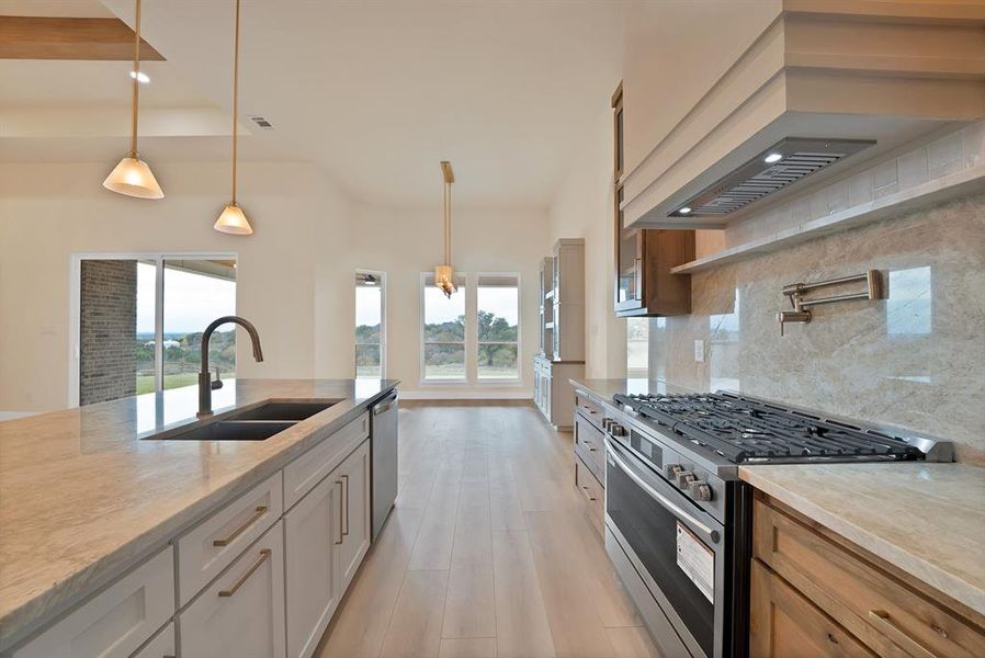 Kitchen featuring hanging light fixtures, appliances with stainless steel finishes, backsplash, light stone countertops, and premium range hood Kitchen featuring hanging light fixtures, appliances with stainless steel finishes, backsplash, light stone countertops, and premium range hood