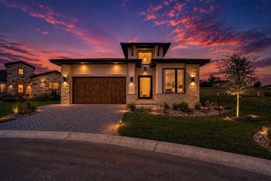 Dramatic lighting illuminates the modern exterior stone accents and custom wood garage door at dusk. Dramatic lighting illuminates the modern exterior stone accents and custom wood garage door at dusk.