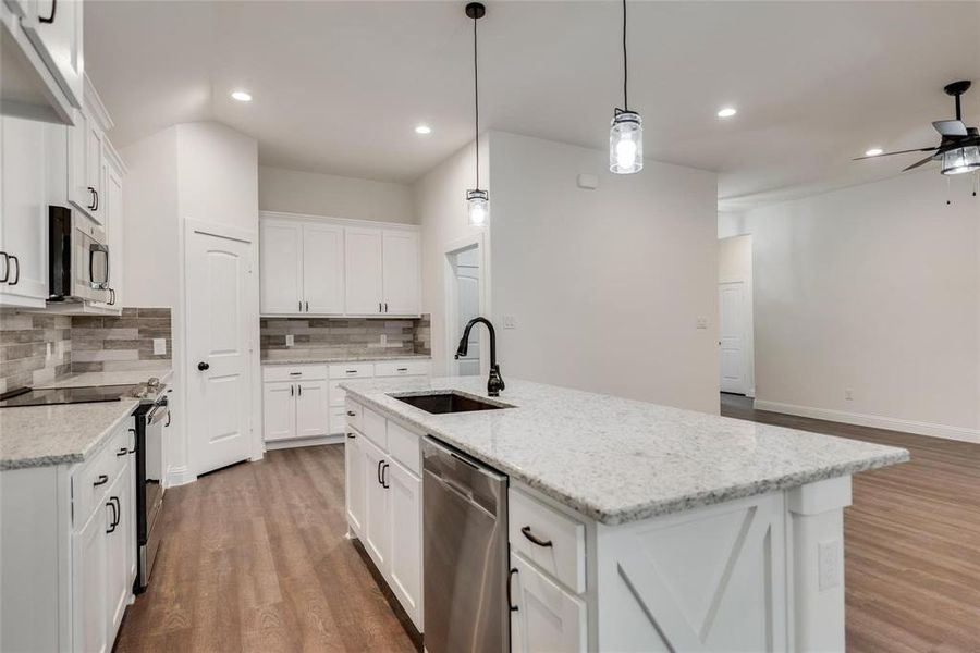 Kitchen featuring stainless steel appliances, white cabinets, a center island with sink, backsplash, and dark wood-type flooring
