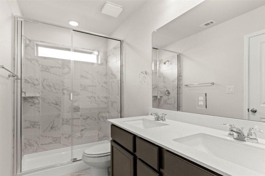 Full bath with a marble finish shower, double vanity, and marble look tiles