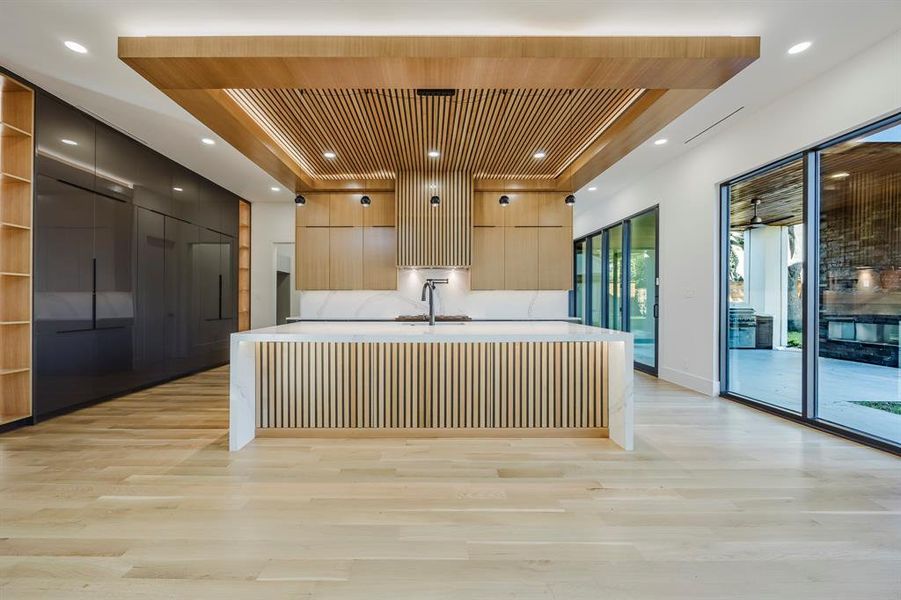 Kitchen featuring modern cabinets, a large island with sink, light stone counters, light brown cabinets, and a kitchen bar Kitchen featuring modern cabinets, a large island with sink, light stone counters, light brown cabinets, and a kitchen bar