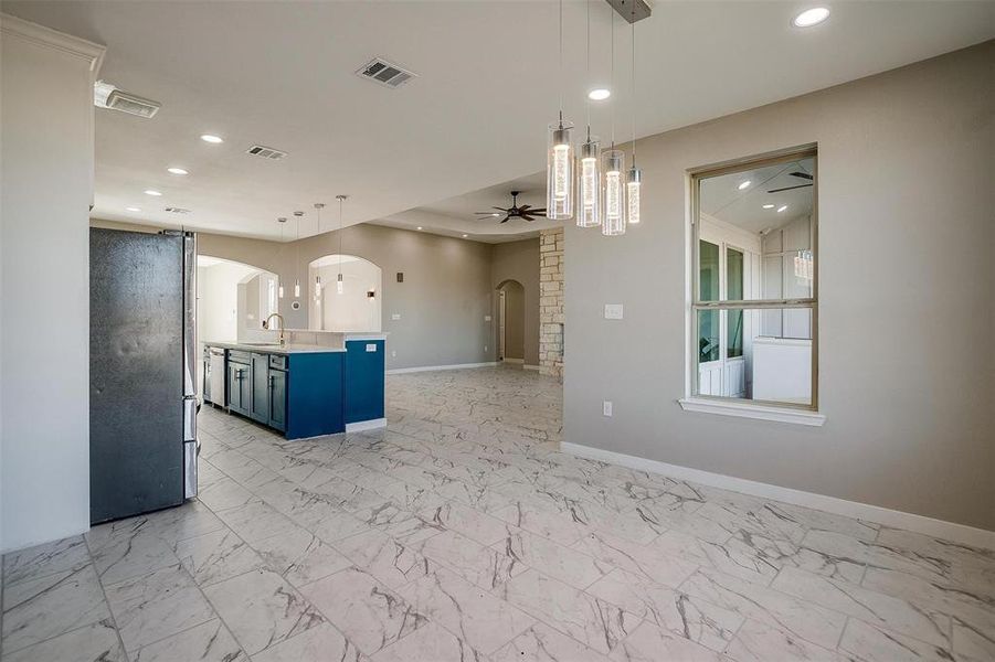 Kitchen with stainless steel fridge, ceiling fan, blue cabinetry, decorative light fixtures, and a center island with sink