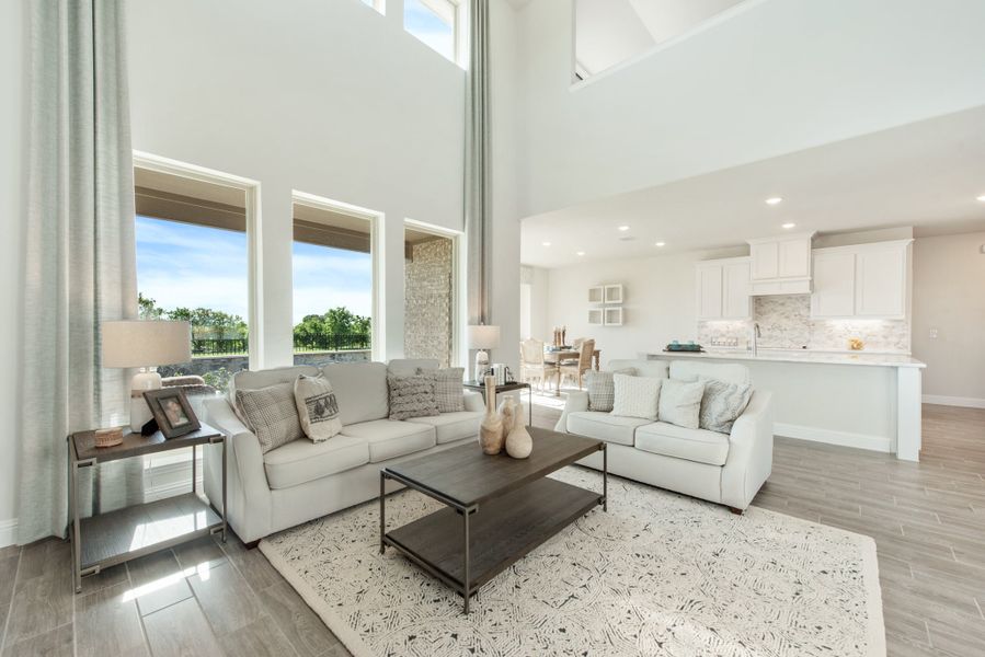 Open-concept living room with two-story ceilings, large windows, and view into white kitchen