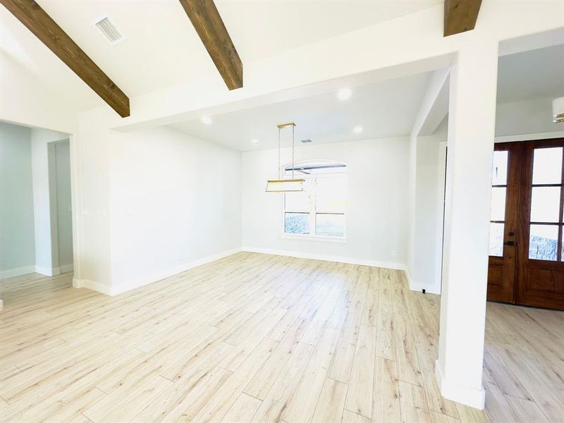 Unfurnished living room with vaulted ceiling with beams, light hardwood / wood-style floors, and french doors