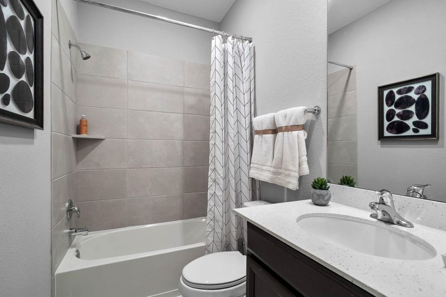 A full secondary bathroom featuring a clean tub/shower combo with stylish tile surround, a single vanity with ample counter space, full width mirrow, and durable, easy-to-clean flooring