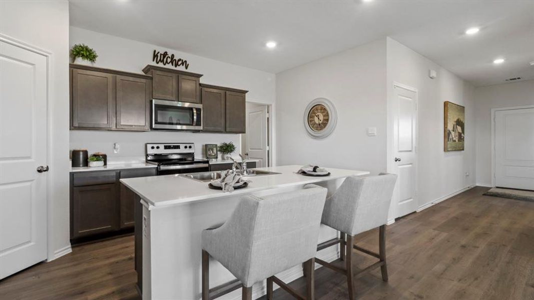 Kitchen featuring dark brown cabinets, dark wood-style flooring, appliances with stainless steel finishes, a kitchen bar, and recessed lighting