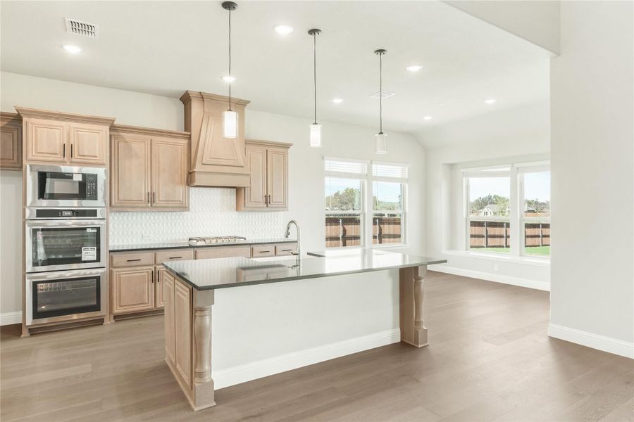 Kitchen with light wood cabinets, large island, dark countertops, and stainless steel double oven Kitchen with light wood cabinets, large island, dark countertops, and stainless steel double oven