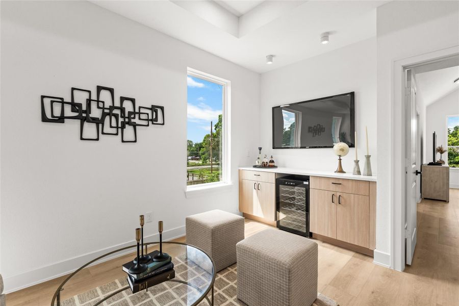 This closer look at the second-floor lounge shows the wet bar and media wall setup. The TV area is placed right above the long countertop, making it easy to host game days. Warm wood cabinets provide plenty of storage, all matching the light oak flooring.