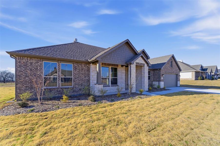 View of front of property featuring a front lawn, covered porch, roof with shingles, driveway, and brick siding
