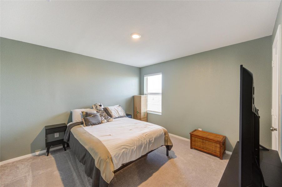 This bedroom features a comfortable layout with soft carpeting, a bed with neutral bedding, and a window providing natural light. The walls are painted a calming shade, and there's ample space for additional furniture.