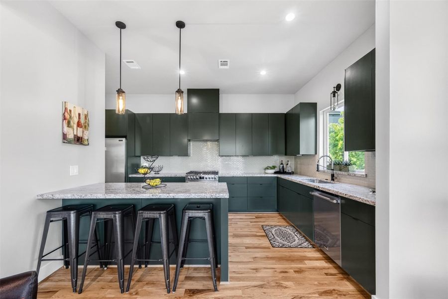 A full-length view of the kitchen showcases the generous layout, ample counter space, a stainless refrigerator, and a window above the sink that floods the cooking area with natural light. The clean, handleless cabinetry gives the space a sleek, contemporary edge.