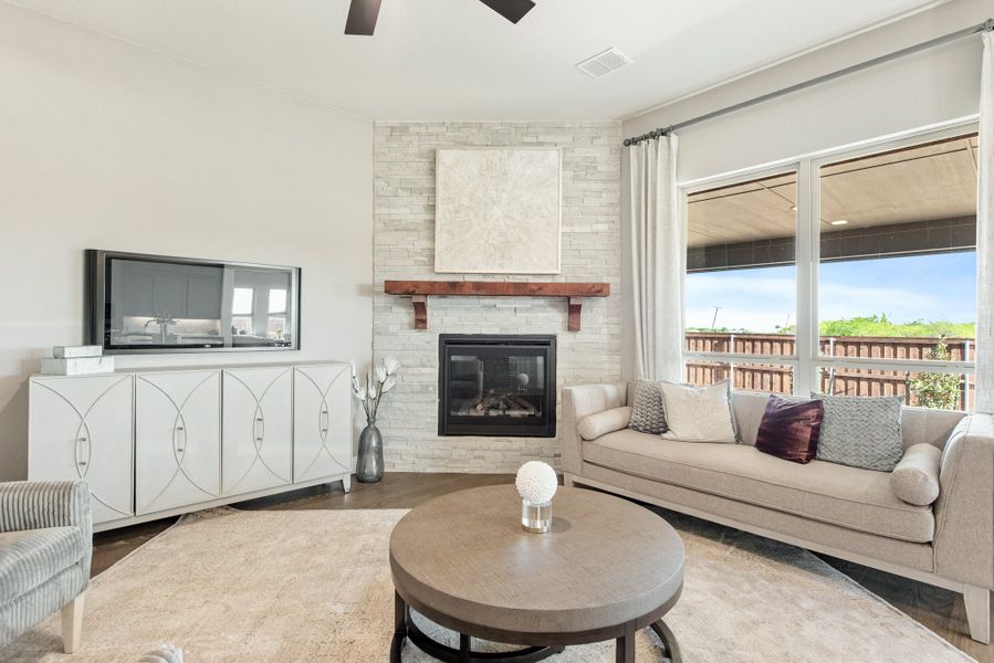 Living room with stone fireplace, wood mantel, gray sofa, round coffee table, and large windows with outdoor view.