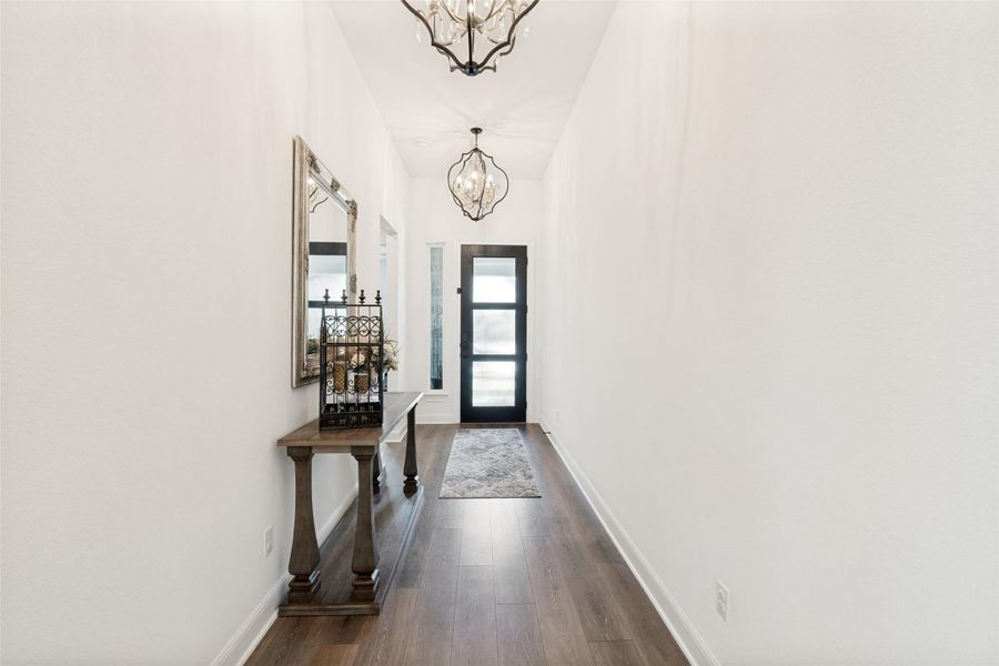 Gleaming wood floors and towering ceilings frame a long hallway leading to the entryway.