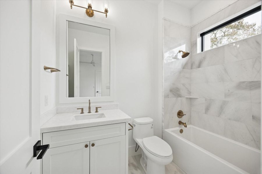 Secondary bath finished with quartz countertops, a custom shaker vanity, and warm brass fixtures for a refined touch. Marble tile tub surround, sleek black framed window, and clean white palette create a bright, timeless space designed for comfort and everyday use.